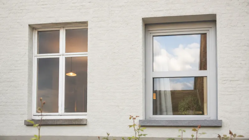 Voorgevel van een Vlaamse rijwoning met een oud enkel glas raam naast een vernieuwd raam met HR-glas en nieuw kozijn