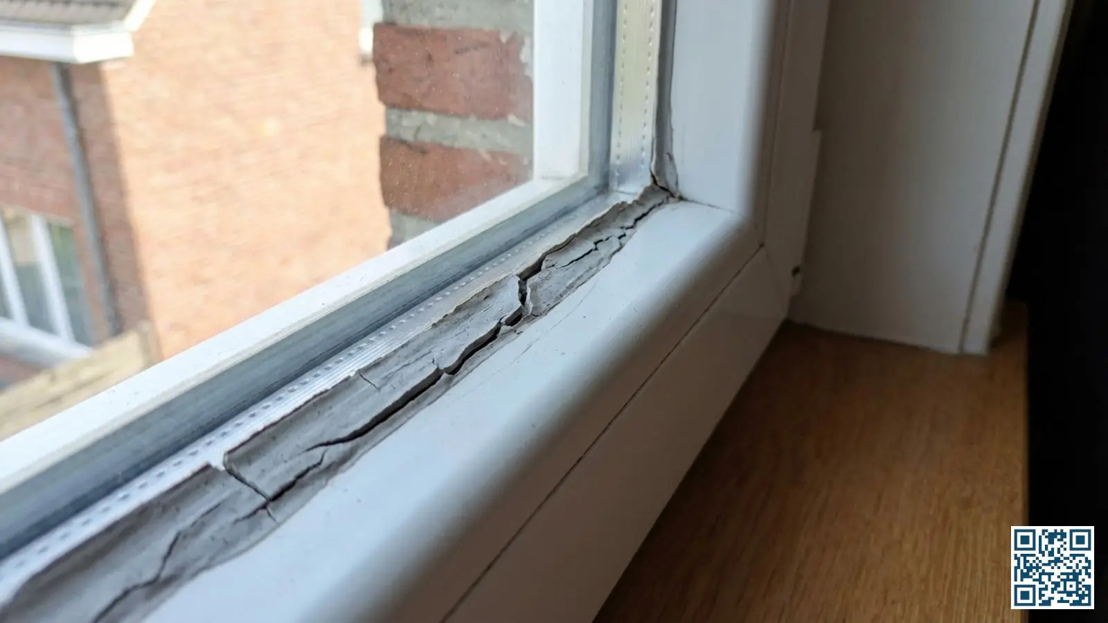 Close-up van verouderde en gescheurde kitranden rond een wit PVC-kozijn met zichtbare scheuren en loslating